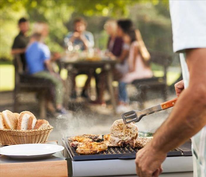 Man cooking food on grill with people in the background.